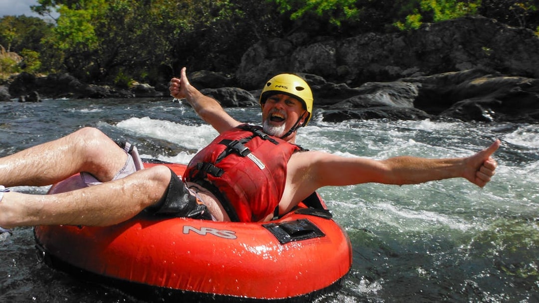 Man enjoying river tubing adventure with thumbs up in a rapid stream.