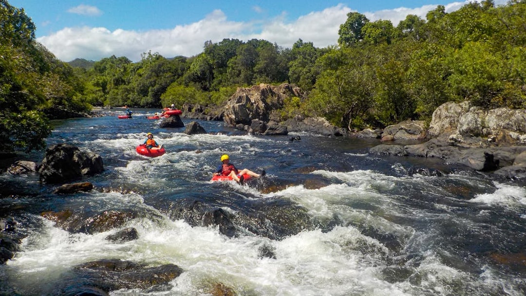 People tubing down a rocky river surrounded by lush greenery.