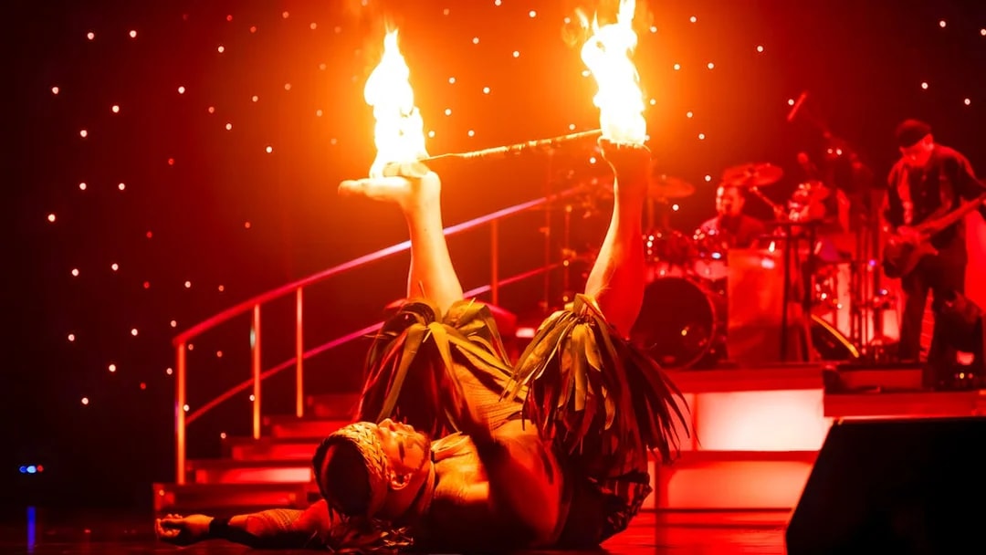 Fire dancer performing with flaming sticks on stage at Rock-A-Hula show.