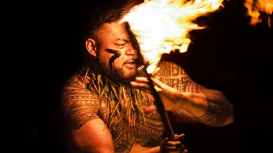 Man with Polynesian tattoos performing a fire dance at night.