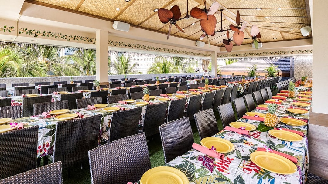 Waikiki Luau Buffet seating area with tropical decor and tables set with yellow plates.