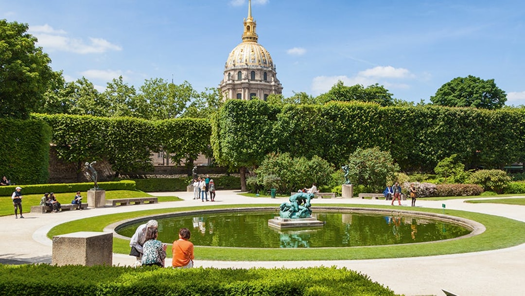 Rodin Museum garden with sculptures and pond, Paris, featuring the golden dome of Les Invalides.