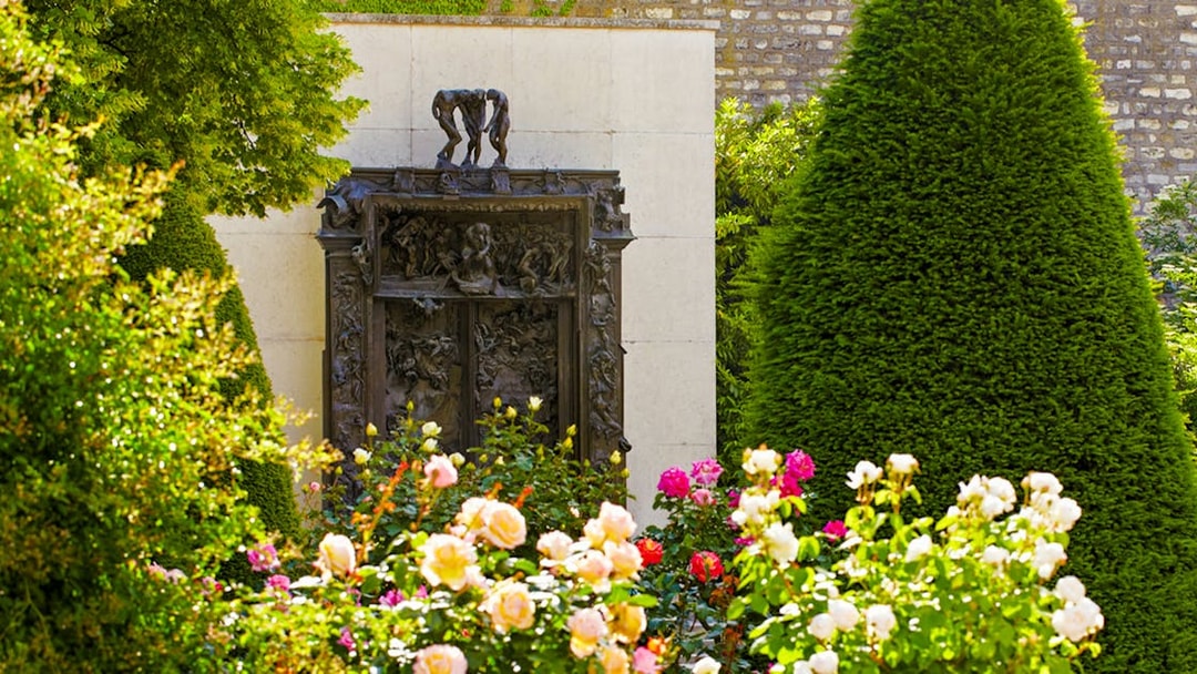 Rodin Museum garden with "The Gates of Hell" sculpture surrounded by flowers and greenery.