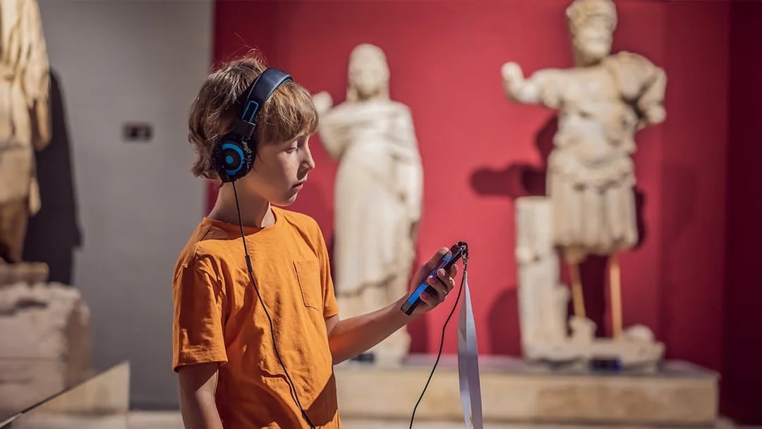 Child with audio guide exploring statues at Accademia Gallery, Florence.