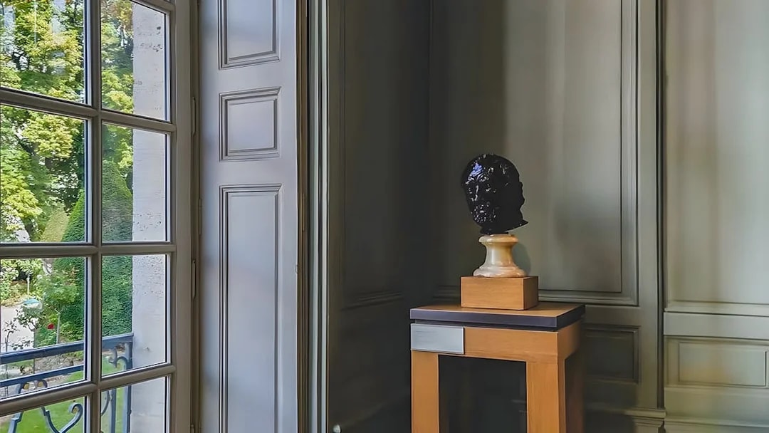 Bust sculpture on display inside Rodin Museum, Paris, near a large window.
