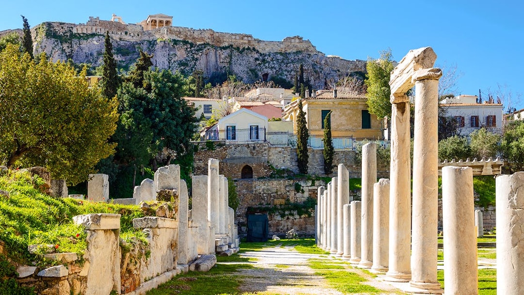 Ancient agora ruins with stone pillars in Athens, Greece, under the Acropolis.