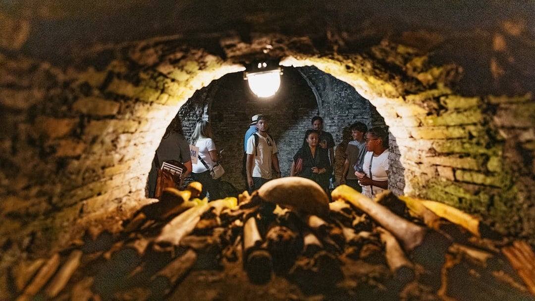 Visitors exploring Roman catacombs with ancient bones in foreground.
