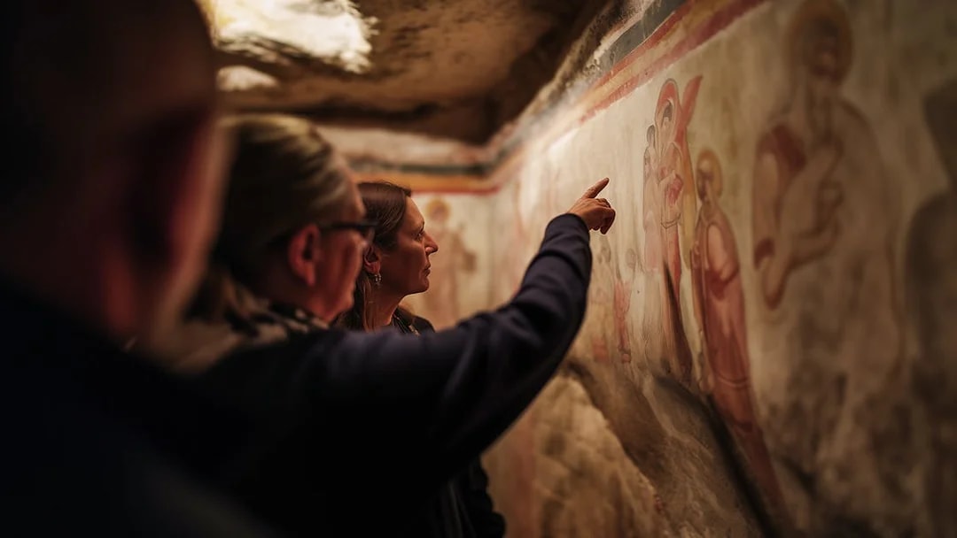 Tour guide explaining ancient frescoes in Roman catacombs.