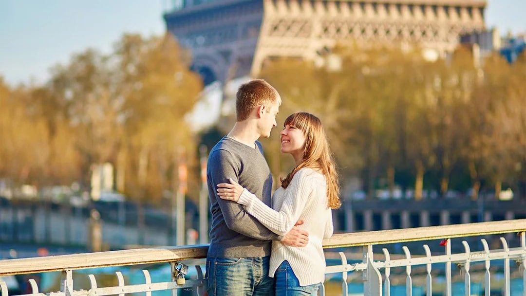 Couple embracing on a Paris bridge with Eiffel Tower in background.