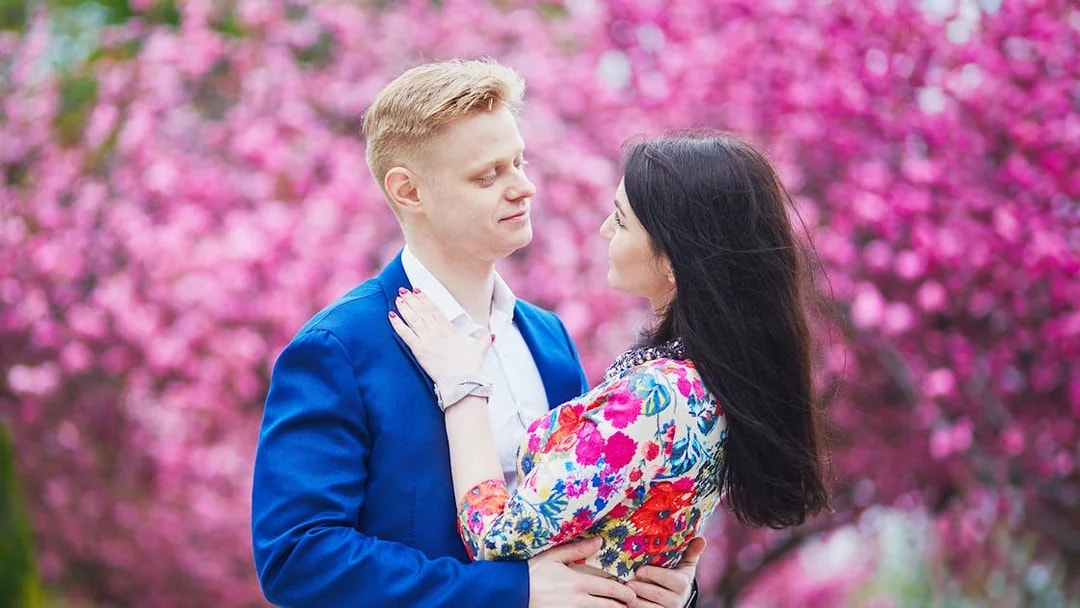 Couple embracing in front of blooming pink cherry blossoms during a romantic photoshoot.