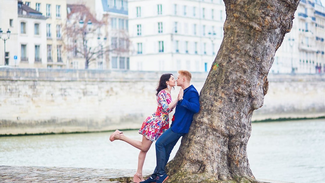 Couple kissing by a tree along the Seine River in Paris.