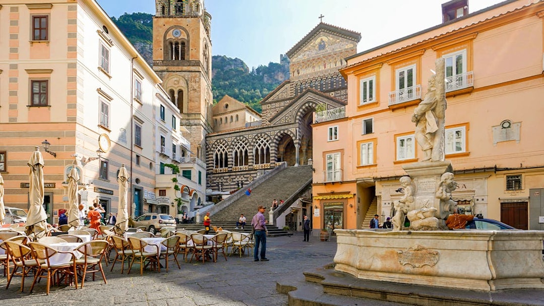 Amalfi Cathedral and fountain in Cathedral Square, Italy, with outdoor café seating.