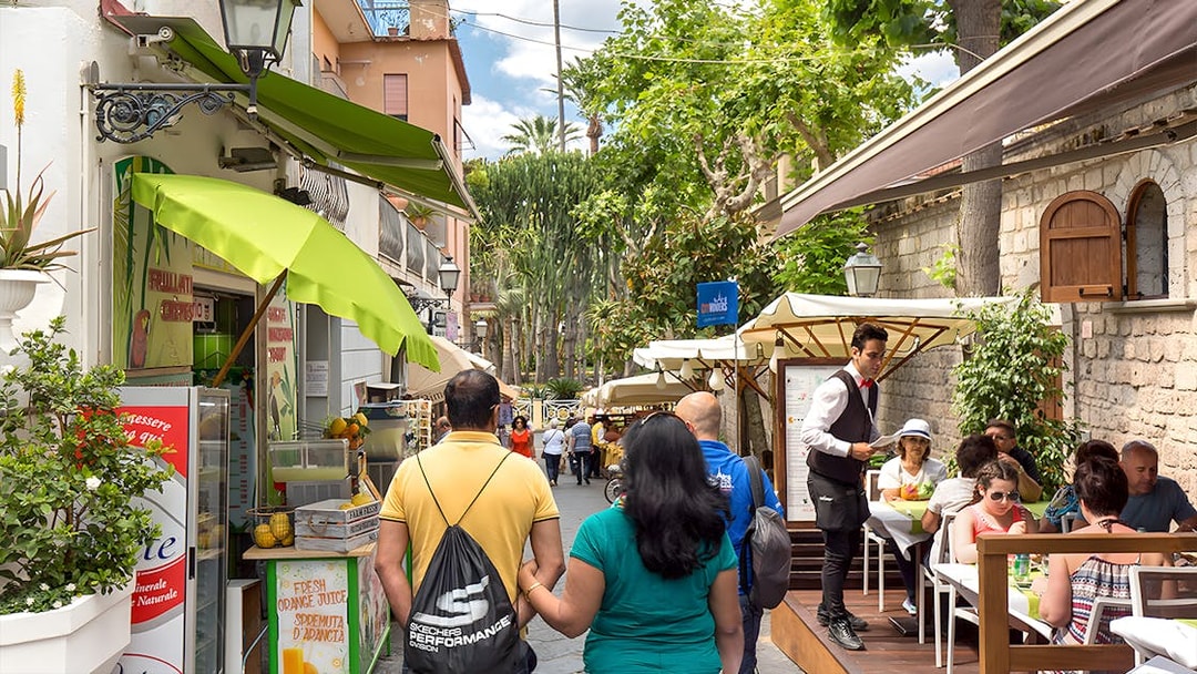 Street cafe in Positano with tourists dining and exploring, part of a guided day trip from Rome.