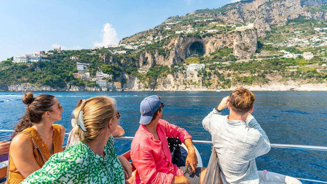 Tourists on a boat viewing cliffs and buildings along the Amalfi Coast near Positano.