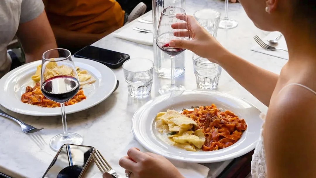 People enjoying pasta and red wine at a restaurant table.