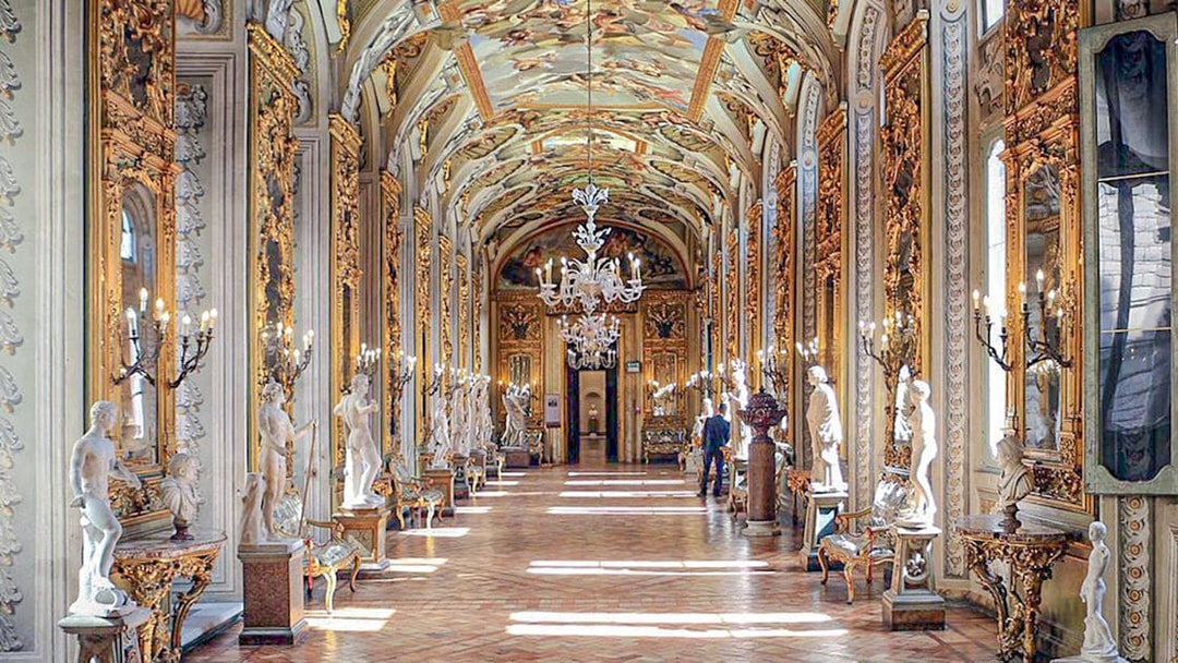 Doria Pamphilj Gallery hall with ornate ceiling, chandeliers, and classical statues.