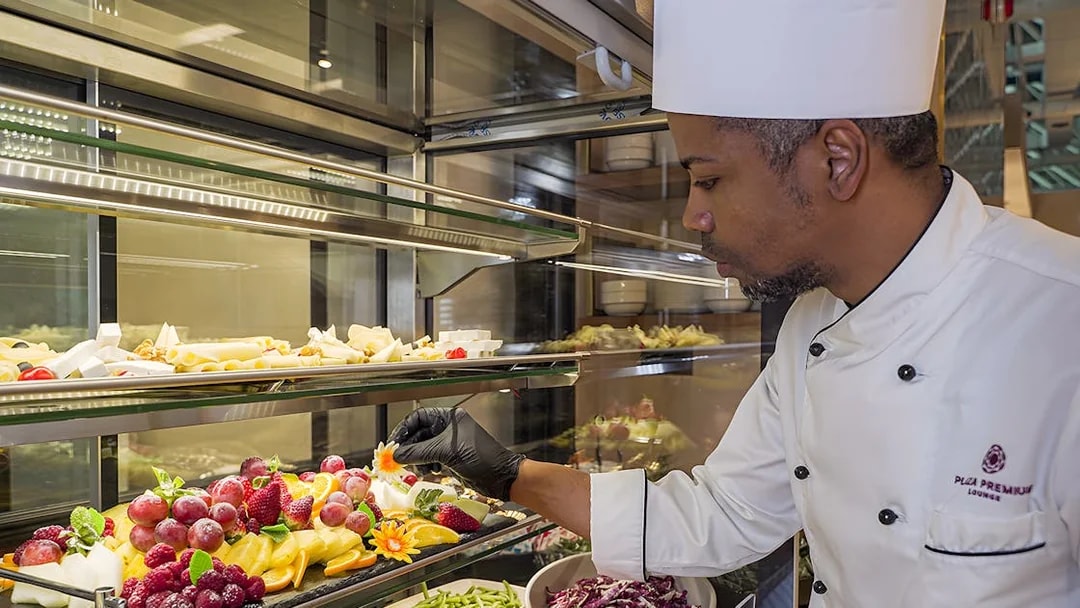 Chef arranging fresh fruit display at Rome Fiumicino Airport lounge.