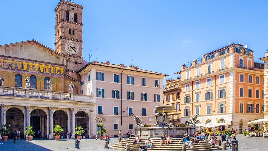 People strolling in Piazza di Santa Maria, Trastevere, Rome, near the basilica and fountain.