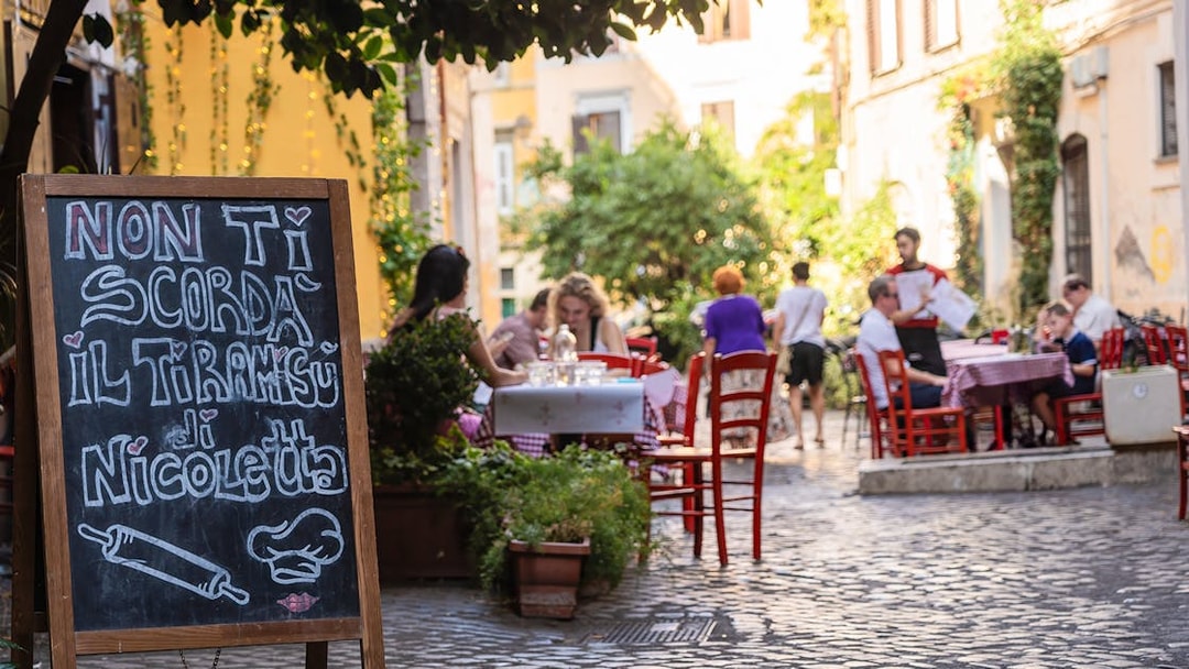 Cobblestone street cafe in Rome with outdoor seating and menu board.