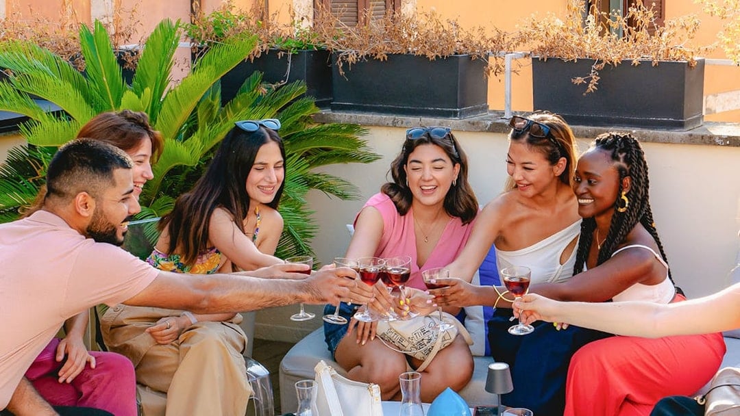 Friends toasting with drinks on a rooftop in Rome.