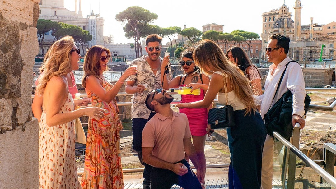 Tourists enjoying drinks together in Rome with historic buildings in the background.