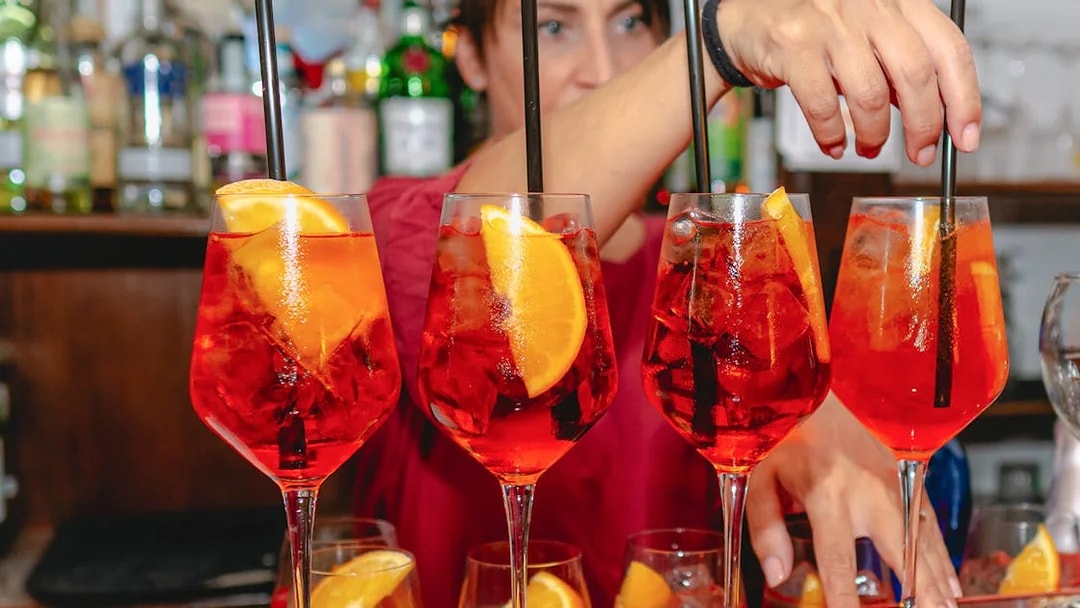Bartender preparing Aperol Spritz cocktails at a bar.