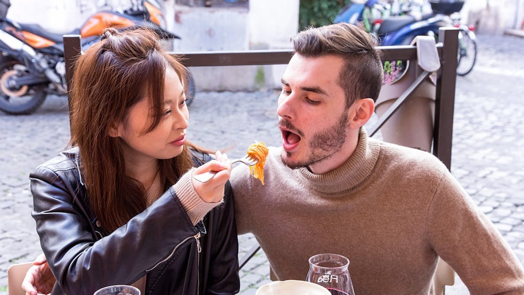 Couple sharing pasta at an outdoor Italian cafe.