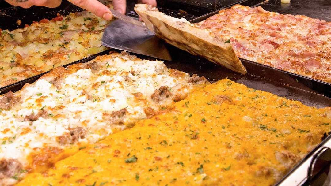 Assorted Italian pizzas being sliced in a bakery.