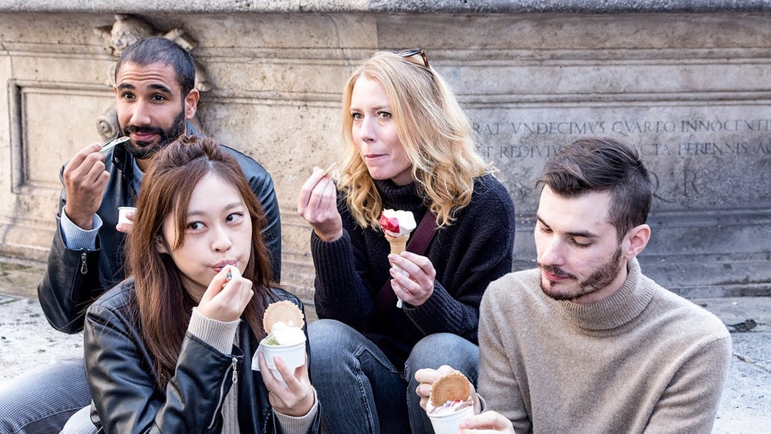 Friends enjoying gelato near a historic stone wall.