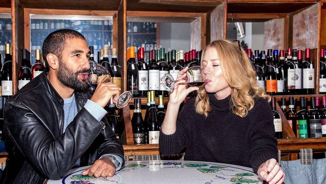 Friends enjoying wine at a bar with bottles displayed in the background.
