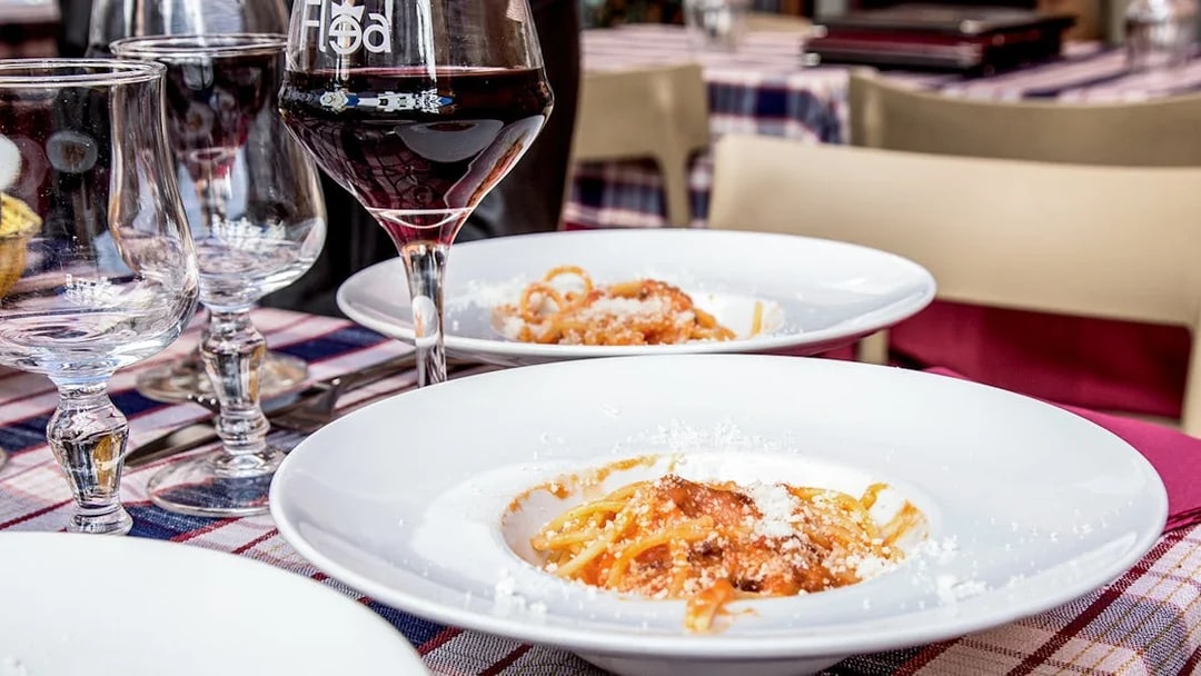 Italian pasta with tomato sauce and cheese served on a table with wine glasses in a restaurant.