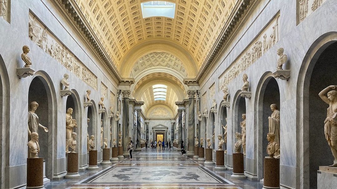 Tourists exploring the Vatican Museums' ornate hallway with classical sculptures in Rome, Italy.