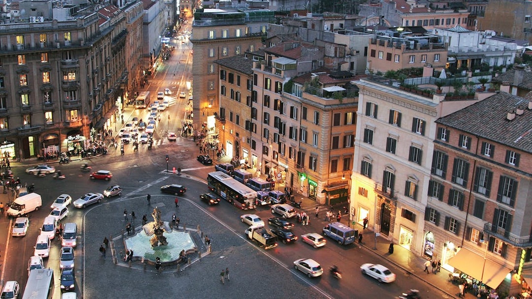 Barberini Square in Rome with Triton Fountain and surrounding buildings at dusk.