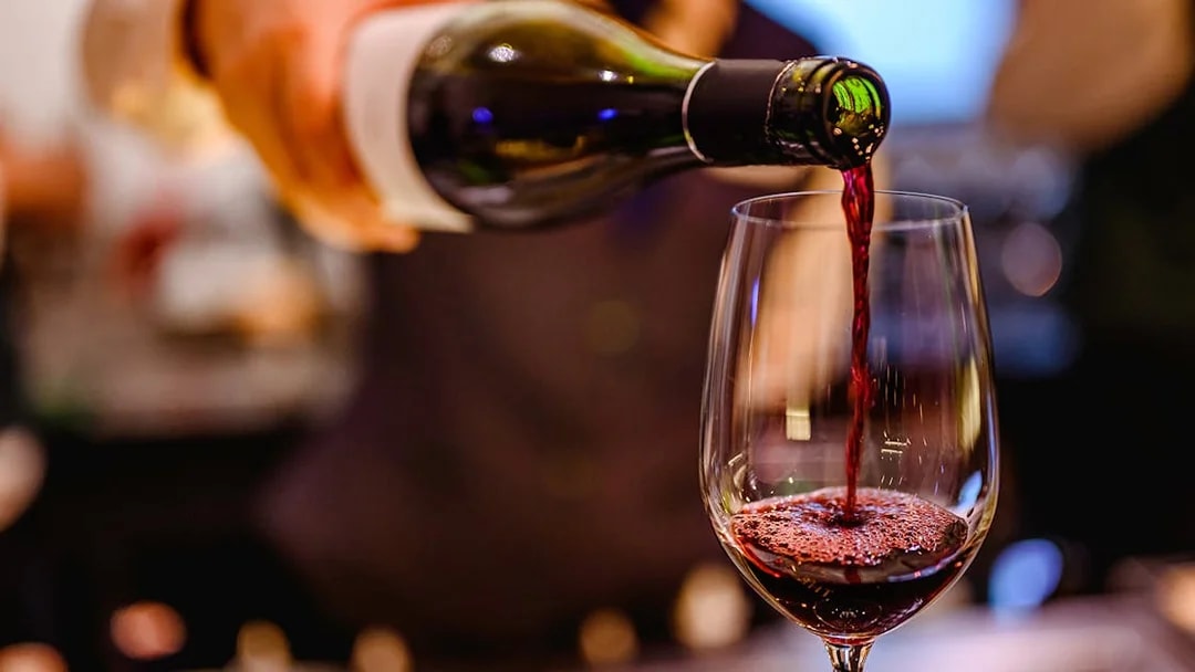 Pouring red wine into a glass at a wine tasting event.