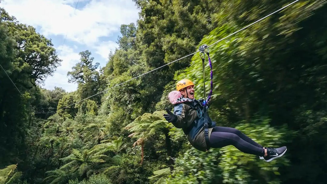 Person ziplining through lush Rotorua forest.