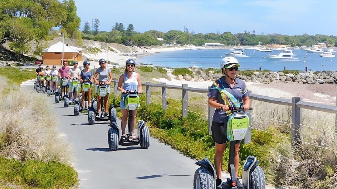 Tourists on Segways exploring Rottnest Island with a ferry visible in the background.
