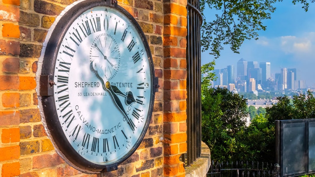 Shepherd Gate Clock at Royal Observatory Greenwich with London skyline in background.