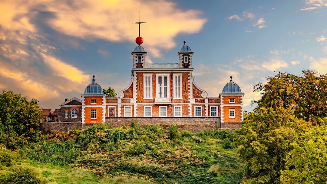 Royal Observatory Greenwich with red brick facade and domed towers against a sunset sky.