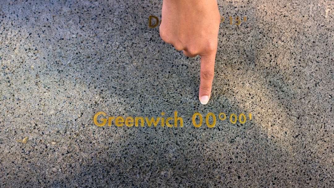 Finger pointing at the Prime Meridian line at Royal Observatory Greenwich.