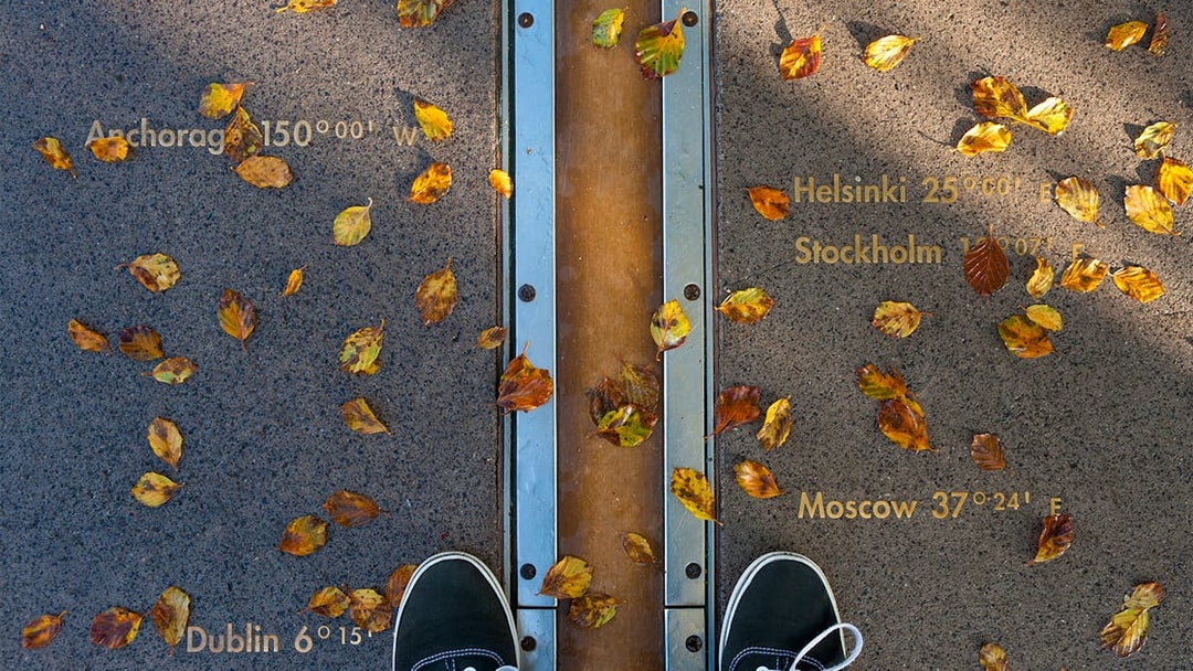 Prime Meridian line at Royal Observatory Greenwich with autumn leaves and city coordinates.