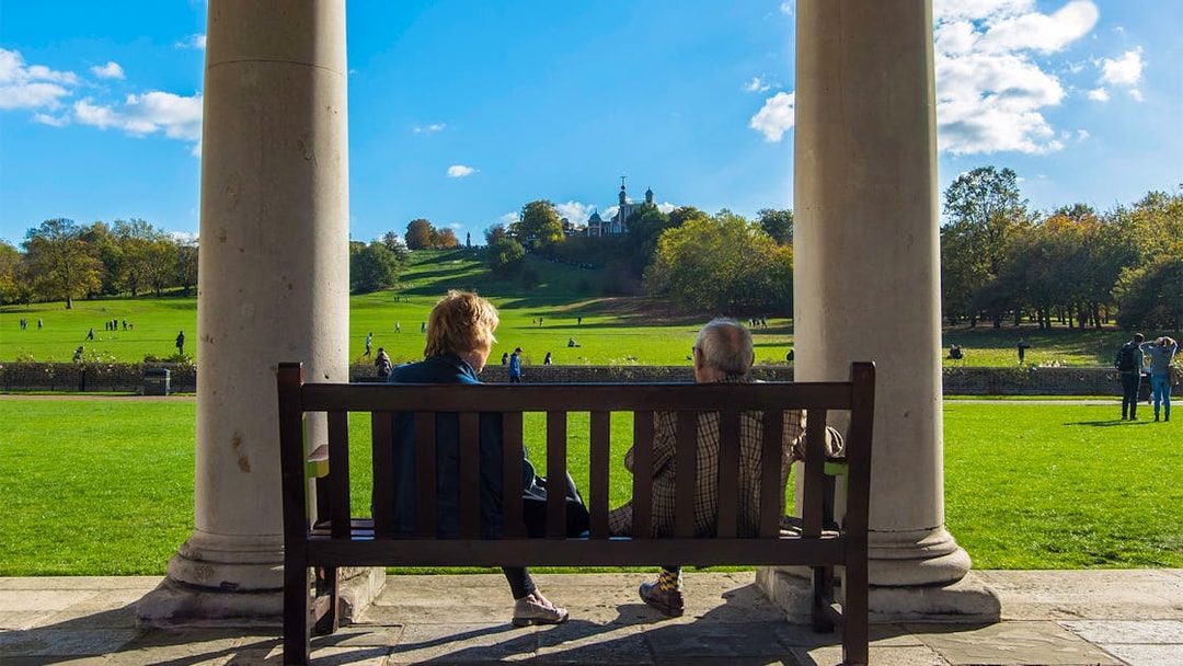 Visitors on a bench overlooking Greenwich Park with Royal Observatory in the distance.