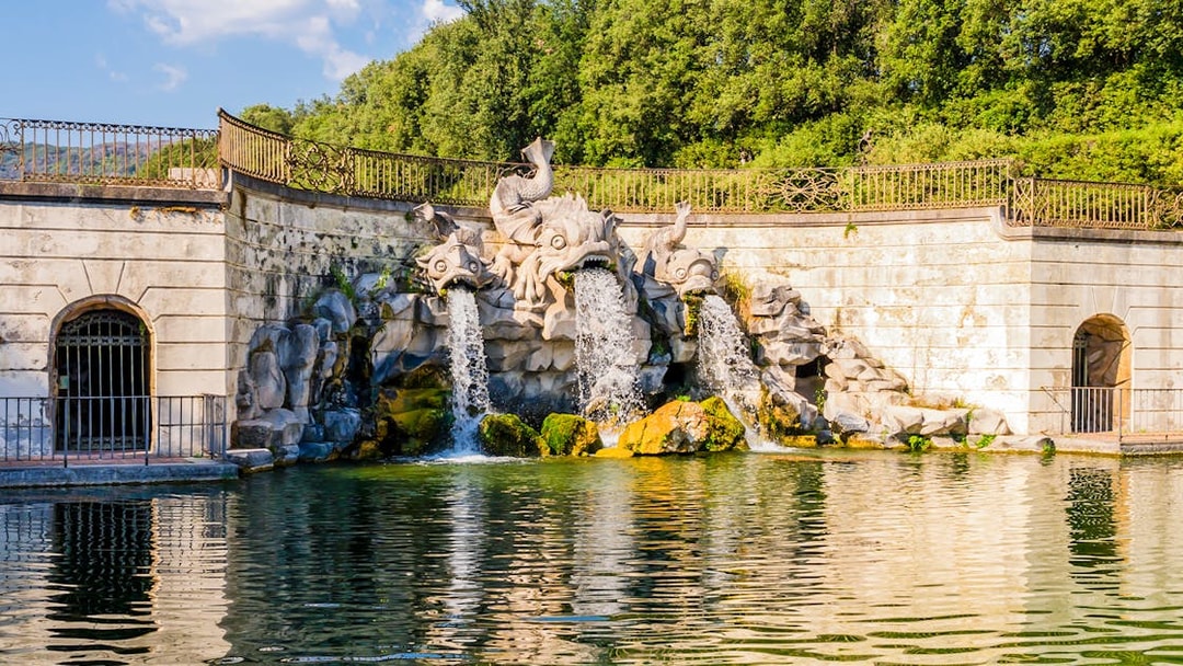 Three dolphins fountain at Royal Palace of Caserta with water flowing into a pond.