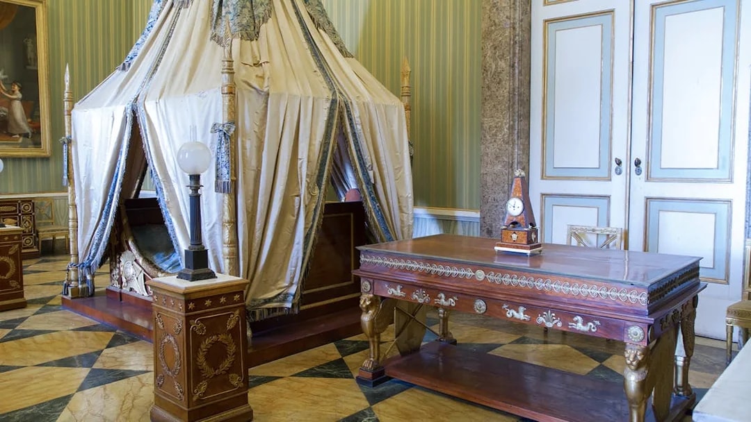 Royal Palace of Caserta interior with ornate canopy bed and decorative wooden table.