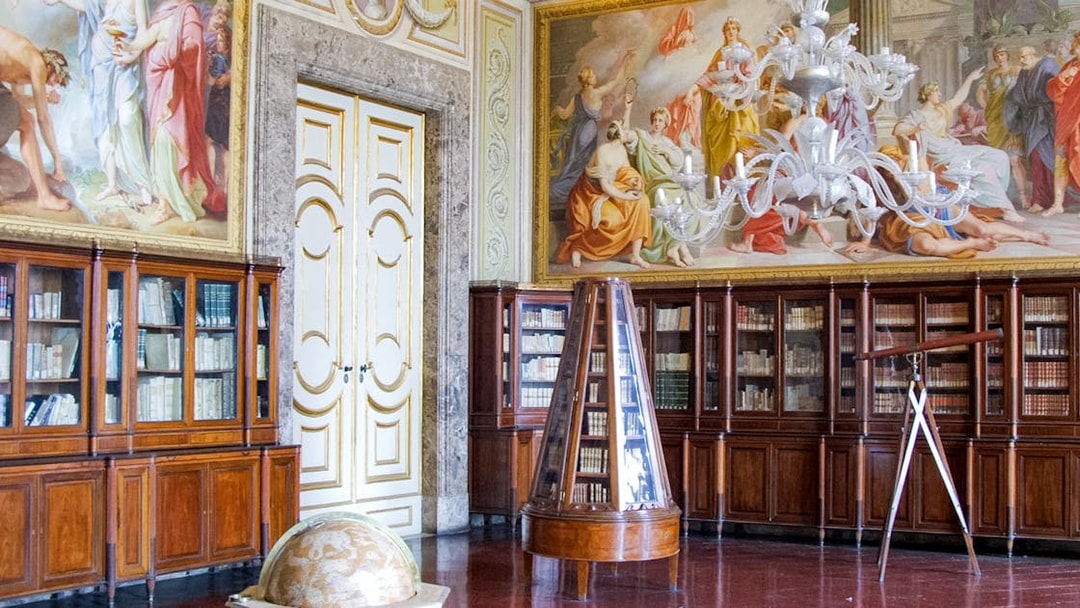 Royal Palace of Caserta library with ornate ceiling frescoes and wooden bookcases.