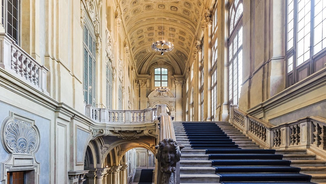 Grand staircase inside Royal Palace Museum with ornate ceiling and large windows.