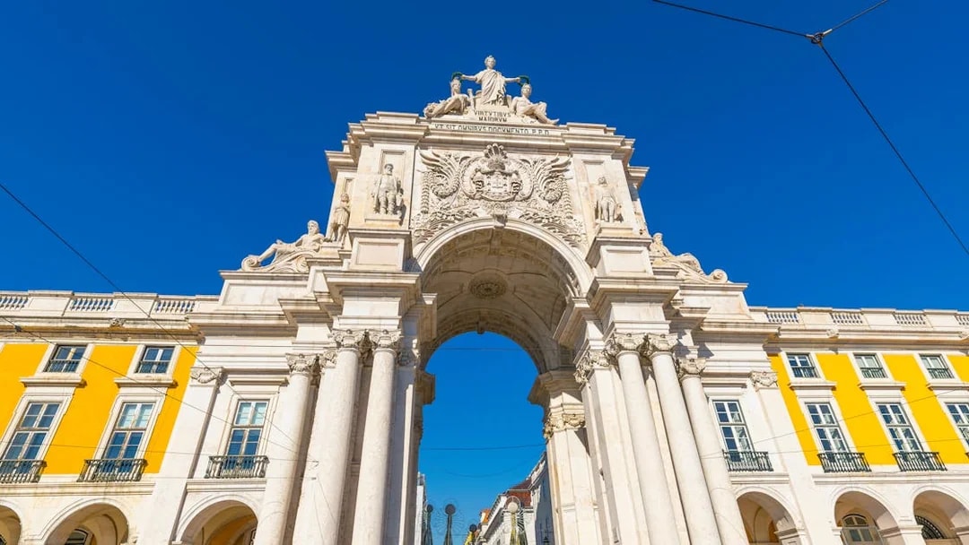 Rua Augusta Arch in Lisbon with detailed sculptures and bright yellow buildings.