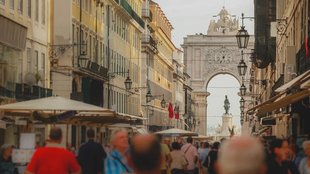 Rua Augusta Arch in Lisbon with bustling street and statue in view.