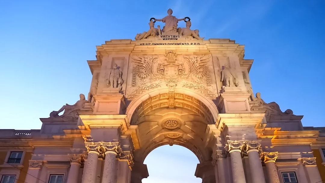 Arco da Rua Augusta in Lisbon at sunset, showcasing detailed sculptures and architecture.