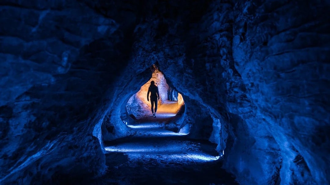 Person walking through illuminated Ruakuri Cave tunnel, New Zealand.