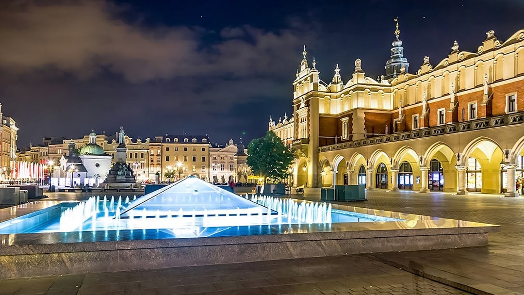 Krakow's Rynek Underground Museum entrance with illuminated fountain at night.